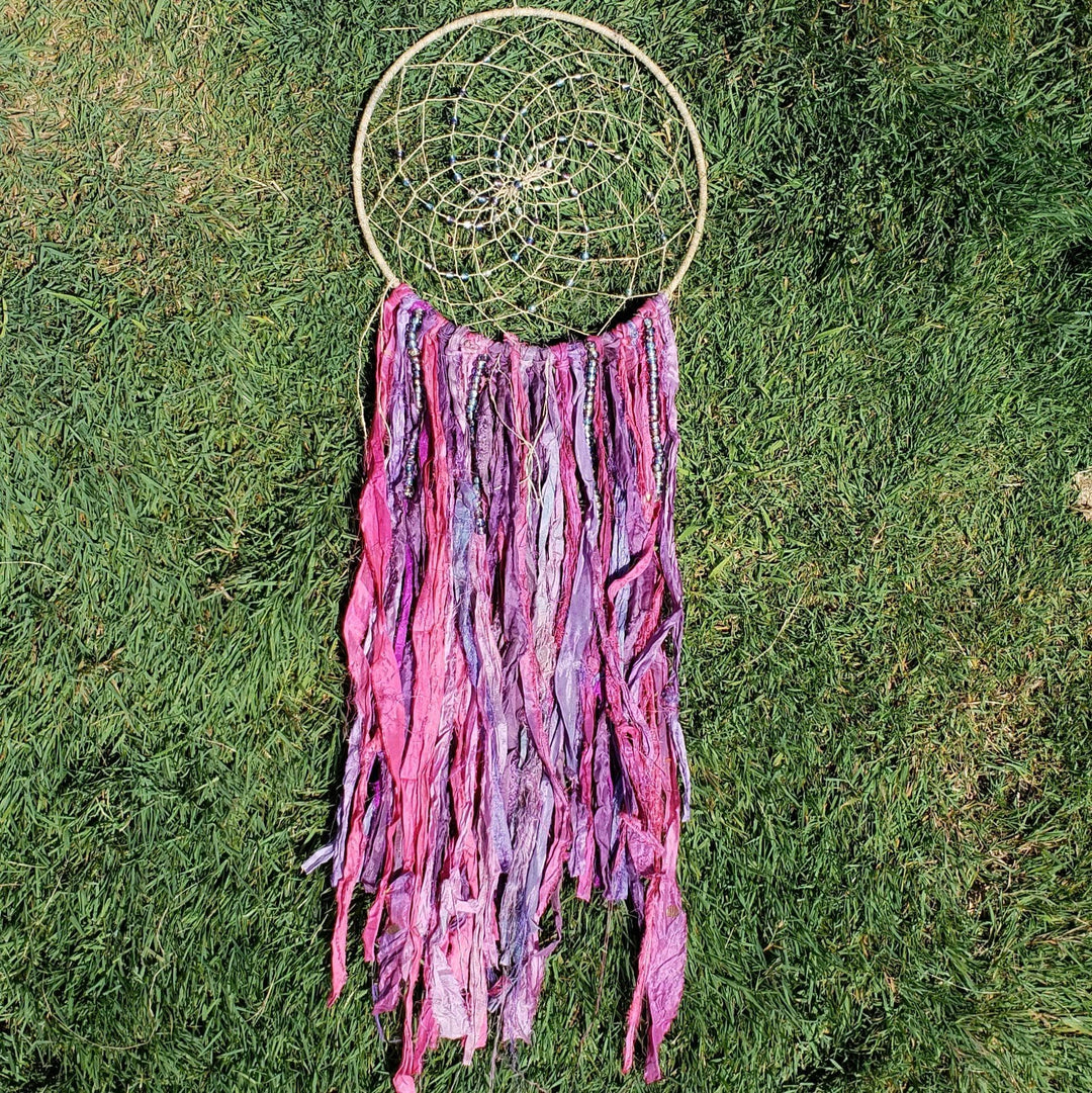 The Simple Dreamcatcher in pinks laying on greenery