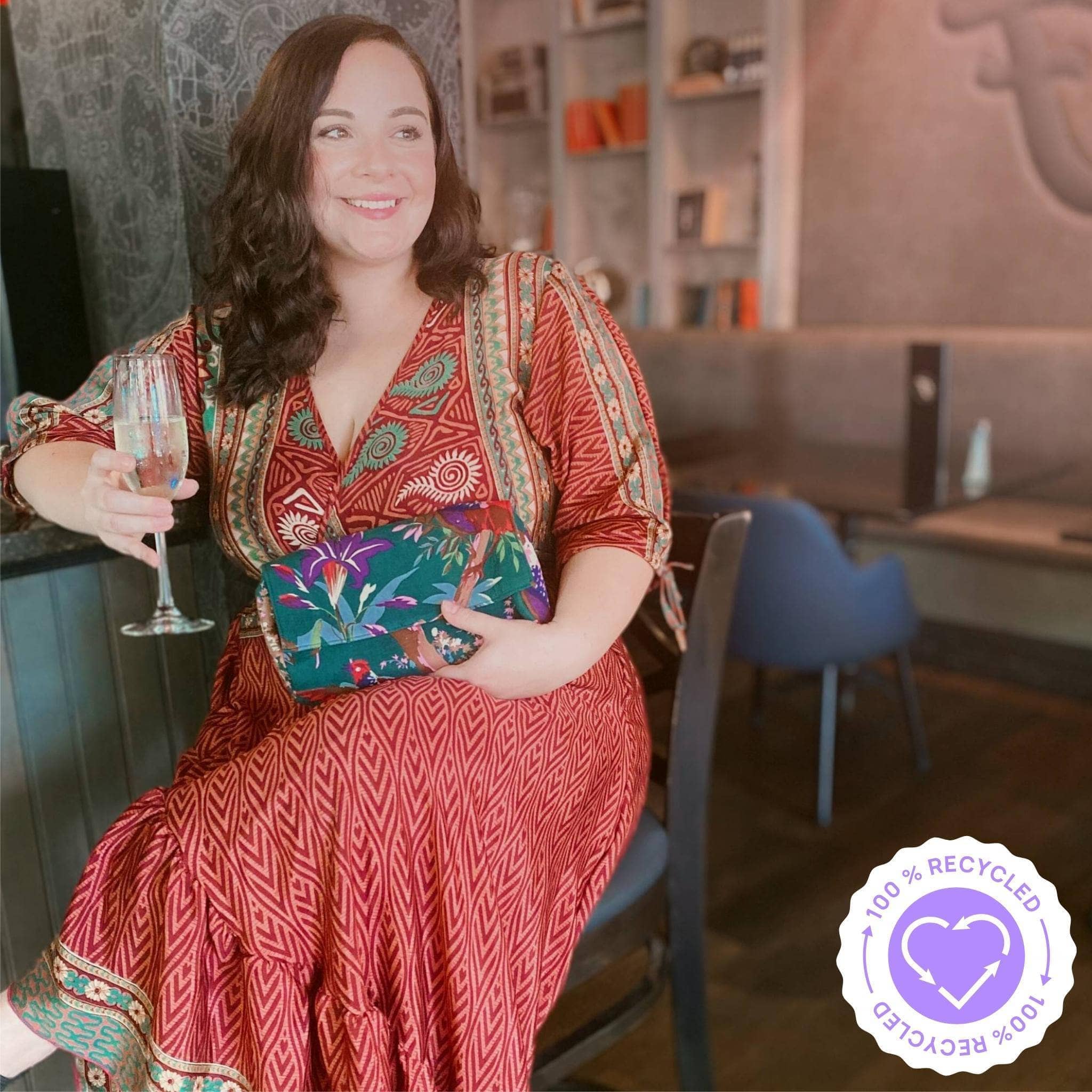 A woman is having a glass of wine at a bar, relaxing after work. Wearing a Zaria wrap dress in warm tones