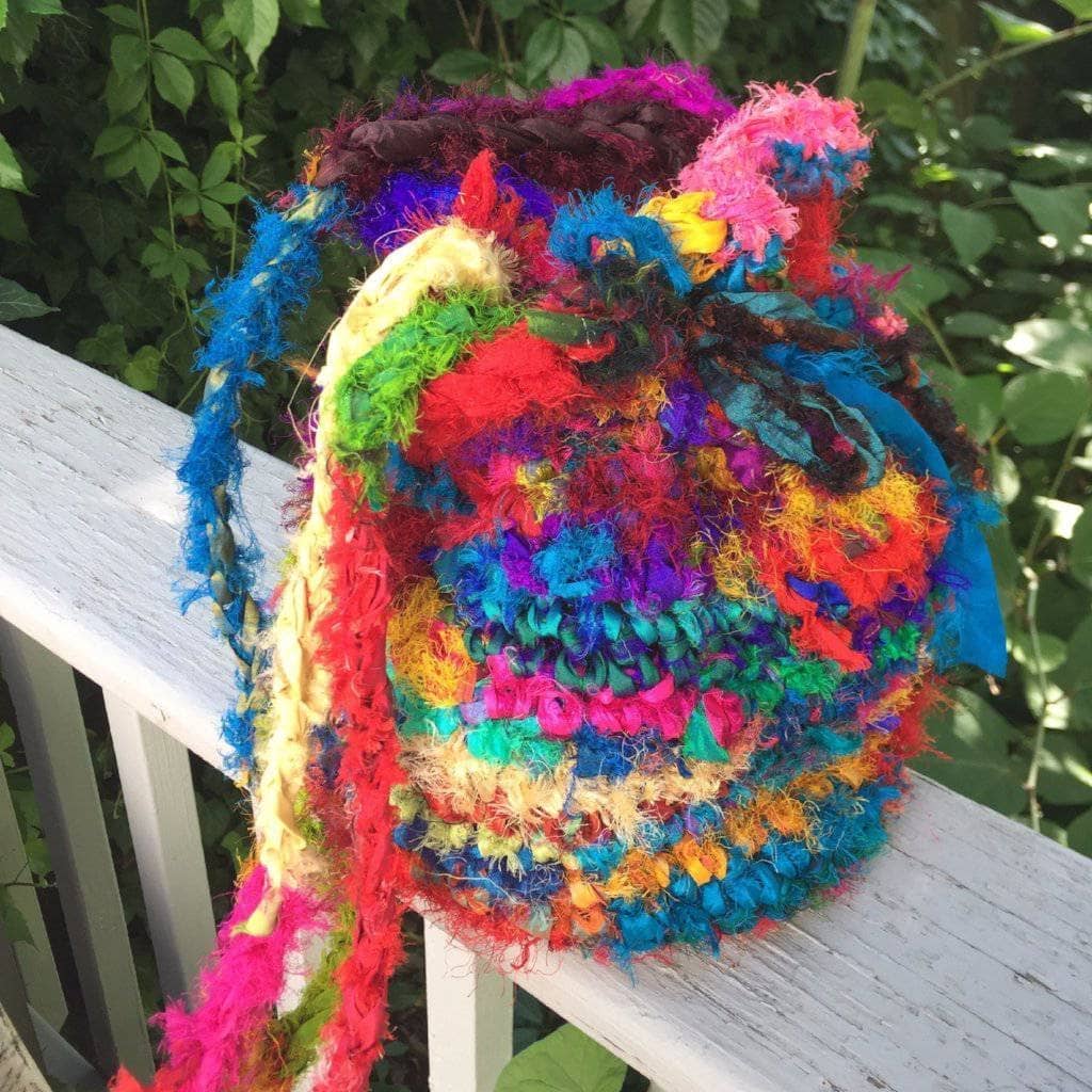 Tibet Jewel Bucket crochet Bag in multicolored ribbon sitting on a wooden fence
