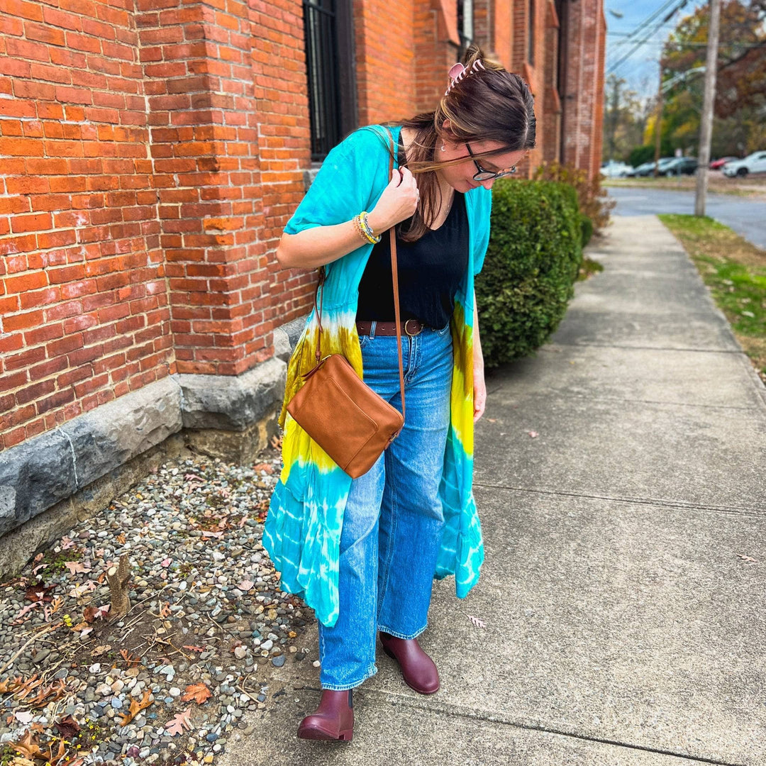 Woman in blue and yellow tie dye wrap dress worn as a duster with a black top and jeans underneath. 