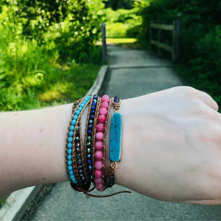 Turquoise and pink wrap bracelet being worn on the wrist outside with a wooded path in the background.