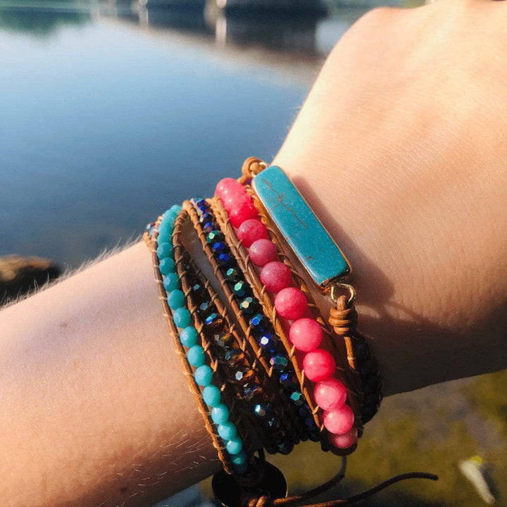 turquoise and pink beaded wrap bracelet being worn on a wrist outside on a sunny dat, water in the backgound.