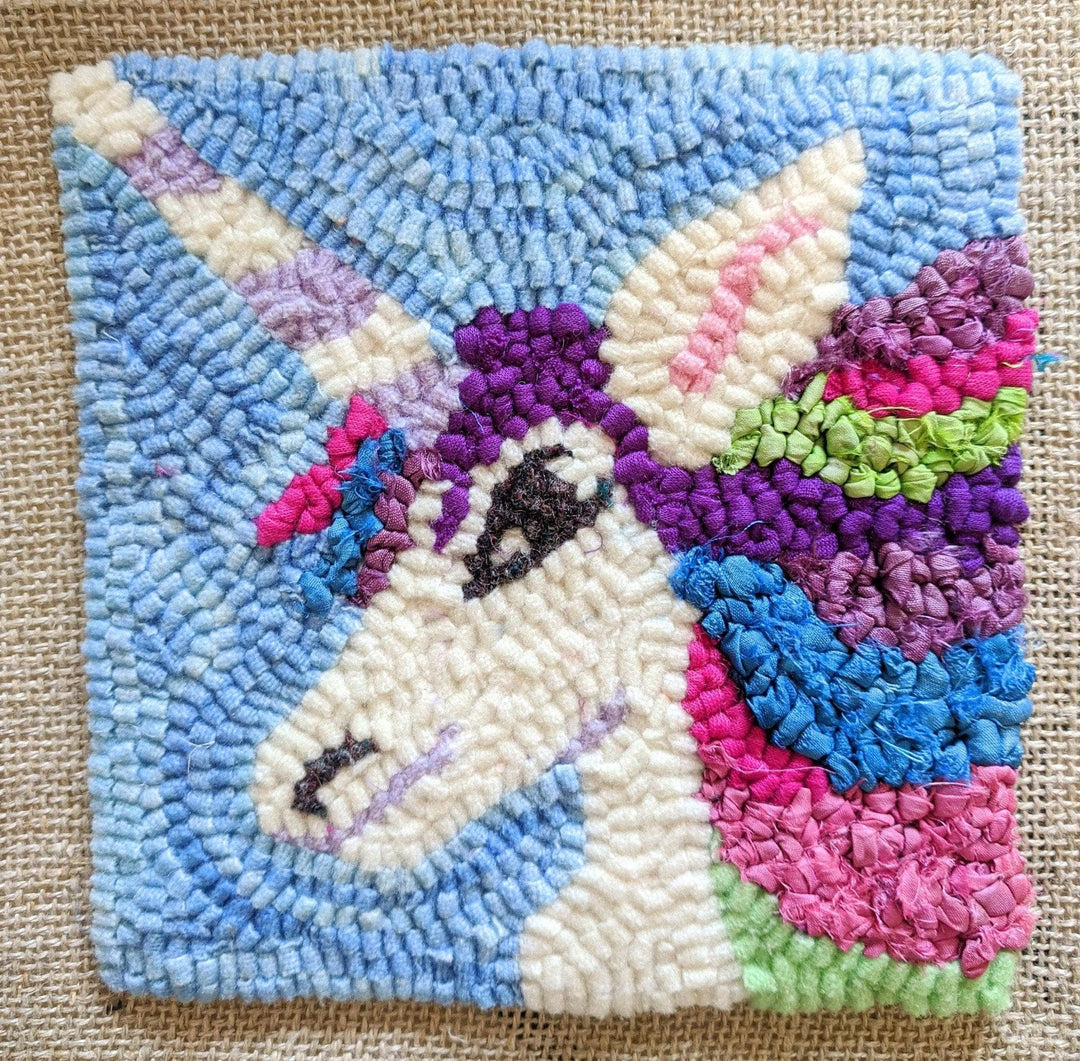 completed unicorn rug hook kit on beige canvas. White unicorn with multicolor mane and horn with blue sky background.