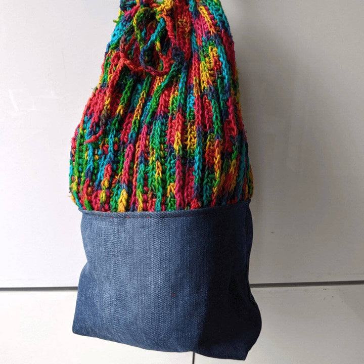 Denim Bag with a rainbow crochet top and handles on a white background