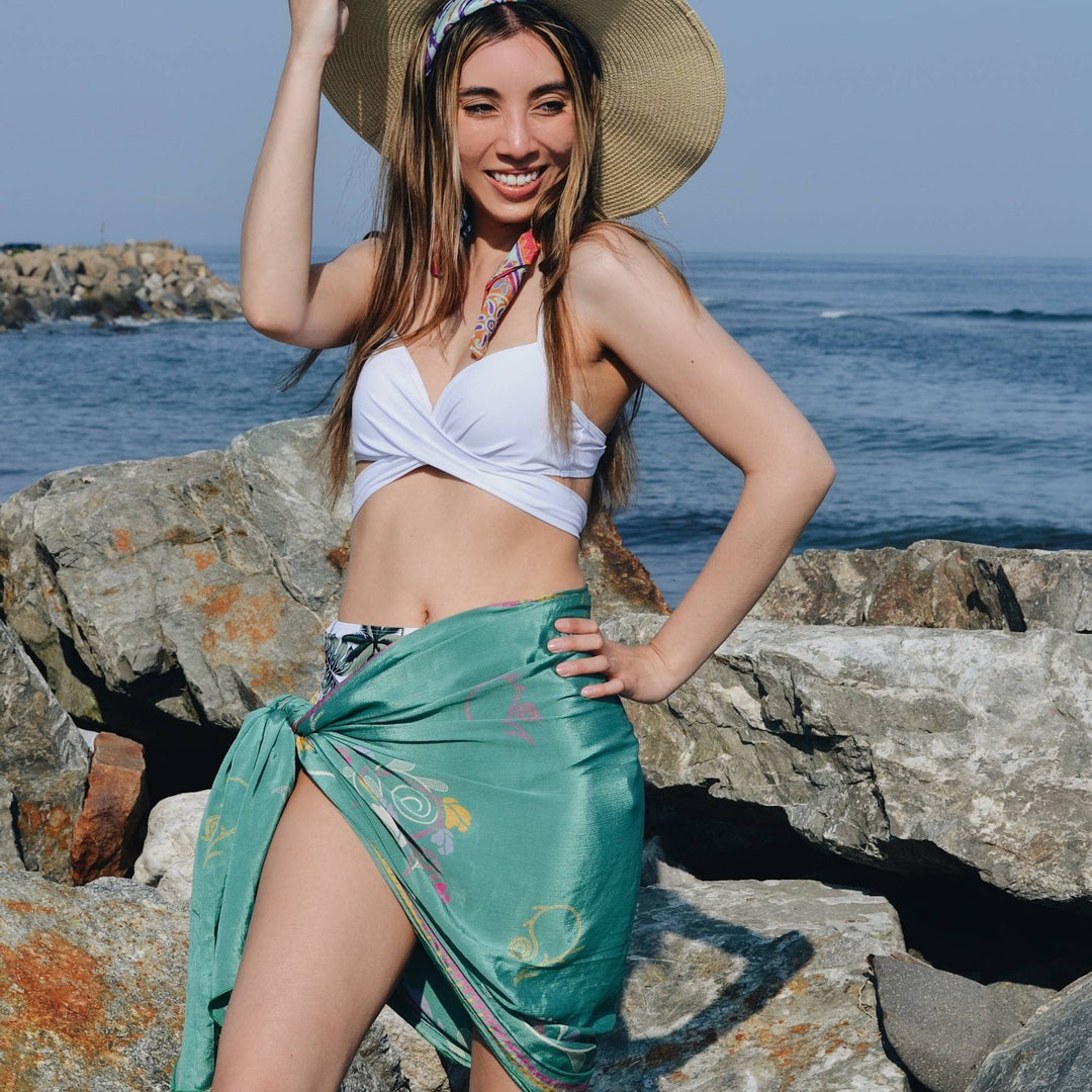 Model is wearing a teal one of a kind sari silk sarong scarf in front of the ocean. 