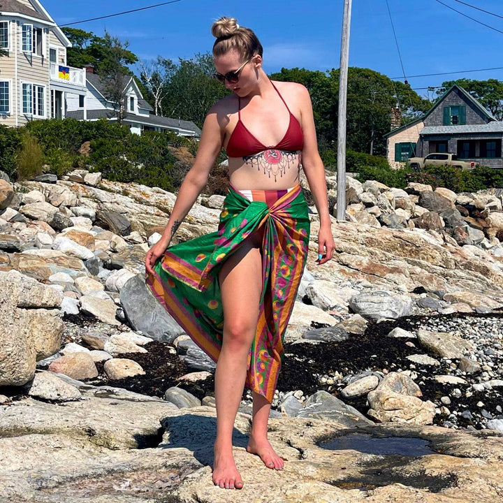 A model standing on some rocks by the ocean wearing an emerald green sari silk beach sarong.