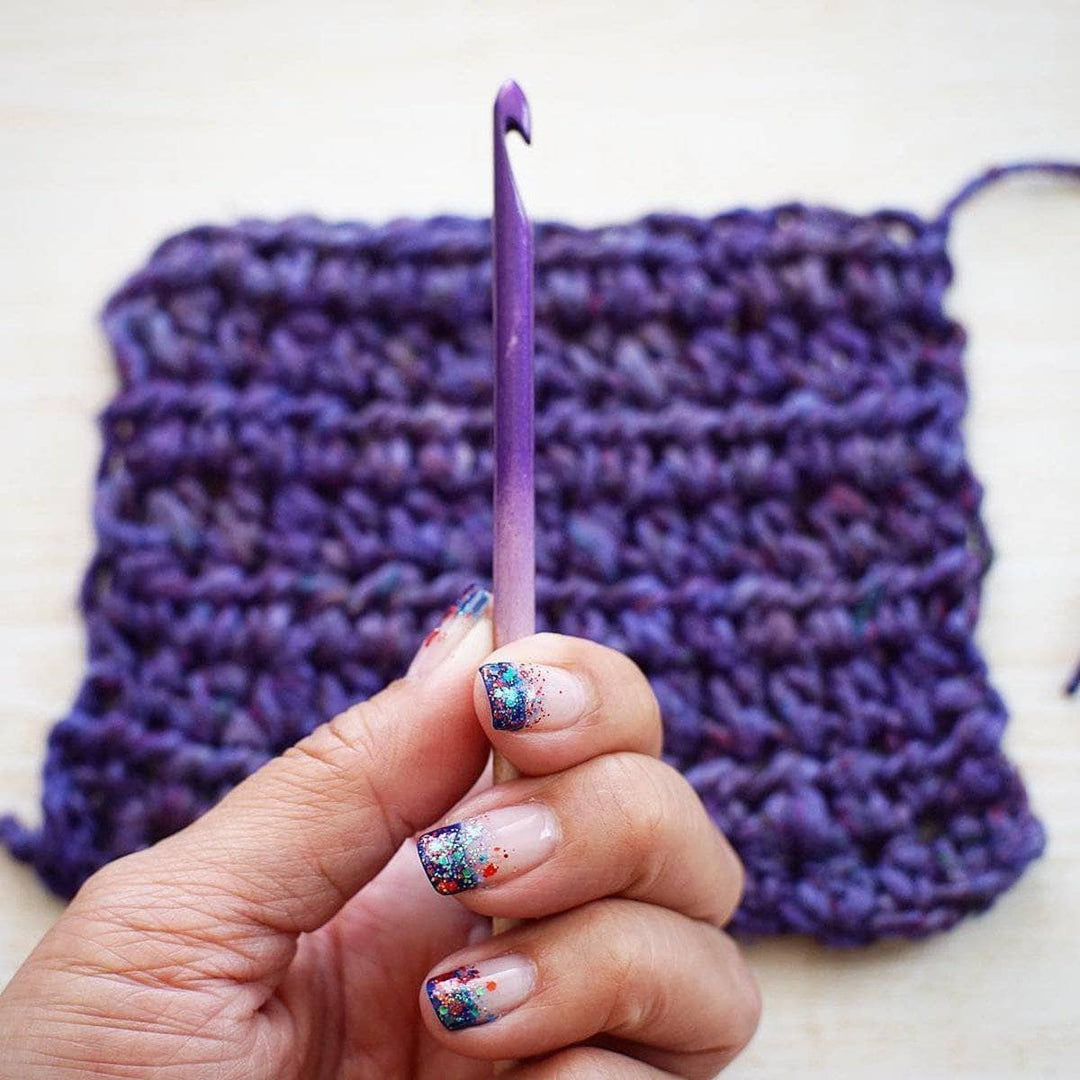 Woman's hand holding US 8/5mm Ombre Crochet Hook over a purple crochet project
