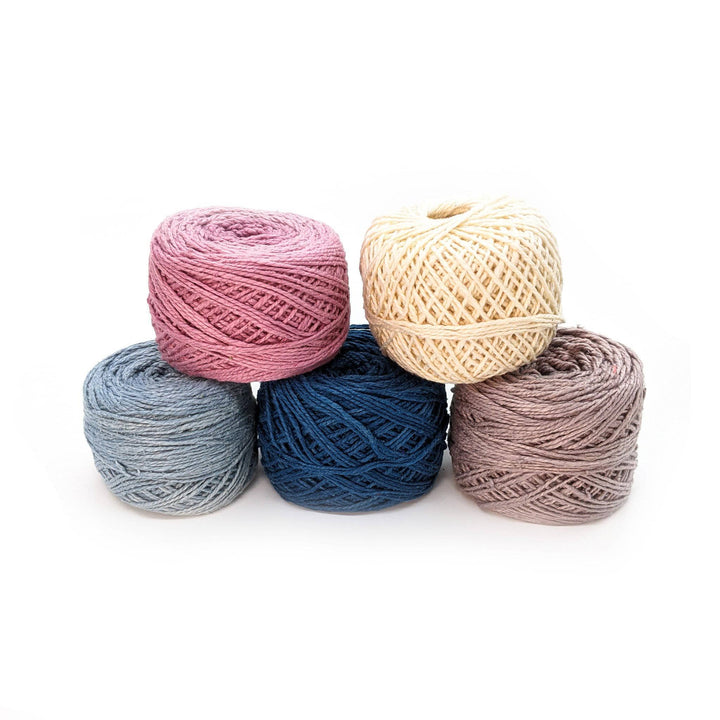 5 cakes of 2 ply herbal dyed recycled silk yarn in the winter frost colorway in front of a white background. Light blue, dark blue, grey, pink, undyed.