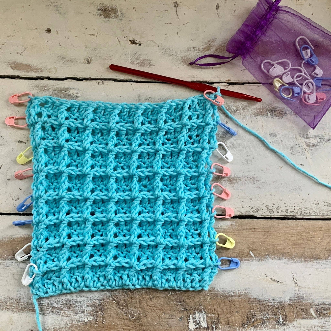 in progress photo of blue crocheted waffle stitch washcloth in front of distressed wood background. 