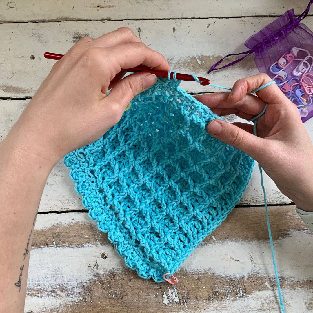 in progress photo of person crocheting a blue waffle stitch washcloth in front of a distressed wood background. 