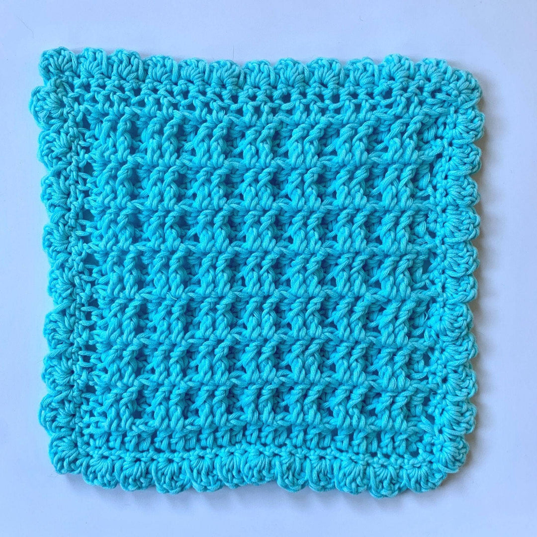 blue crocheted waffle stitch washcloth laid flat in front of a white background.