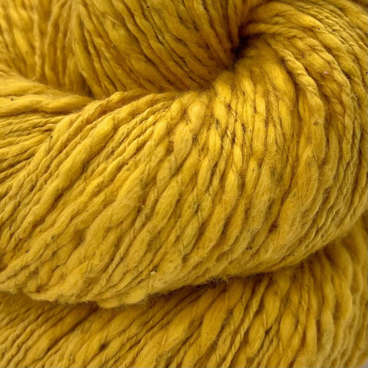 A close up of a skein of goldenrod yellow cotton yarn on a white background