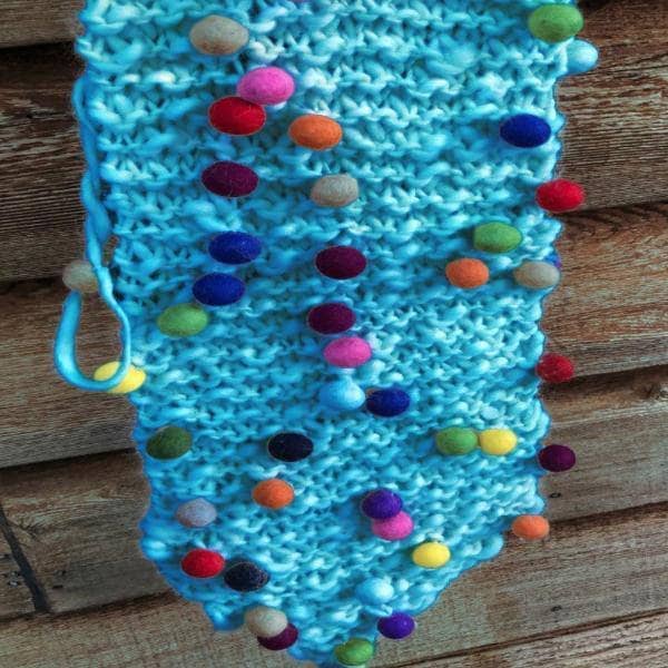 Whimsical Winter knit Wall Hanging in Turquoise hanging in front of a wooden wall