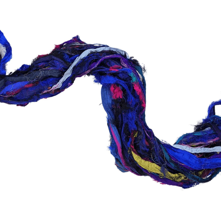 Skein of windswept sari silk ribbon yarn indigo untwisted in front of a white background to show detail. 