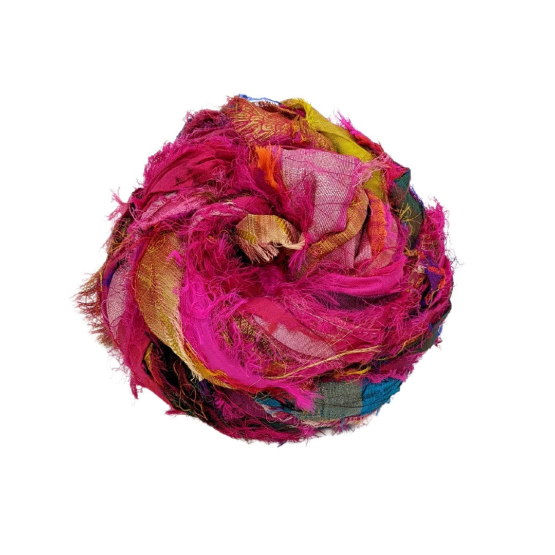 Skein of windswept sari silk ribbon yarn magenta in front of a white background. 
