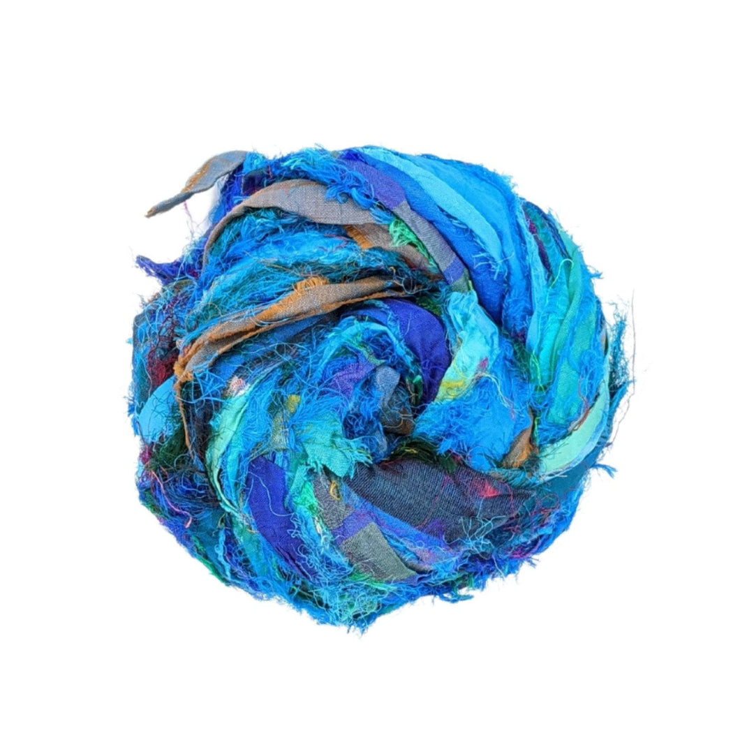 Single skein of windswept sari silk ribbon yarn turquoise in front of a white background. 