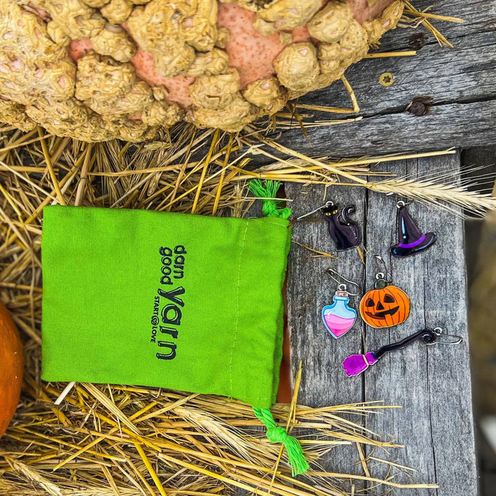 Green darn good yarn drawstring bag laying on some hay next to a pumpkin with the spooky stitch markers. 