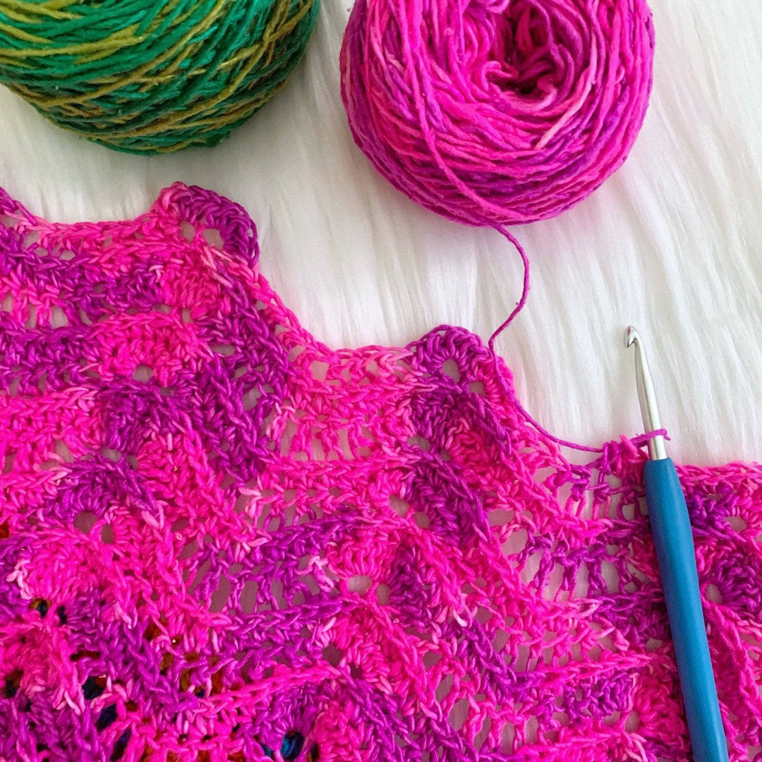 Sea breeze crochet wrap in the rainbow colorway being shown in progress, using the pink yarn in front of a textured white background.