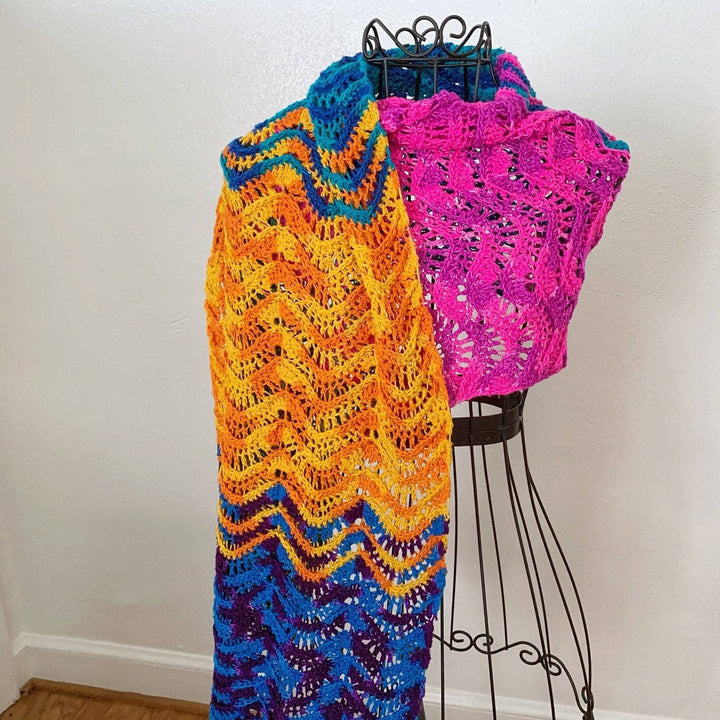 Sea Breeze crochet wrap in the rainbow colorway displayed on a black wire dress form in front of a white background.