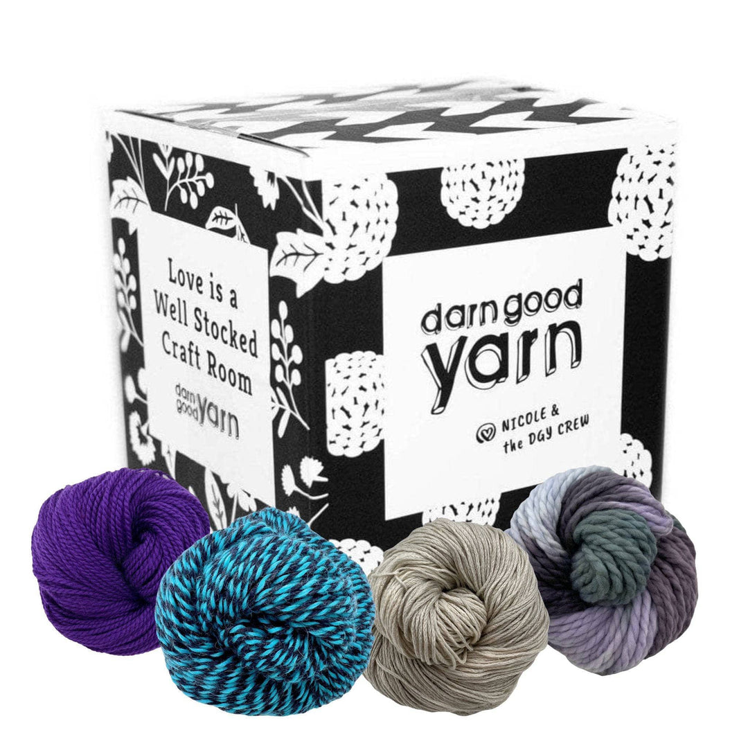 A black Darn Good Yarn branded box sitting on a white background with 4 skeins of wool yarn sitting around it.